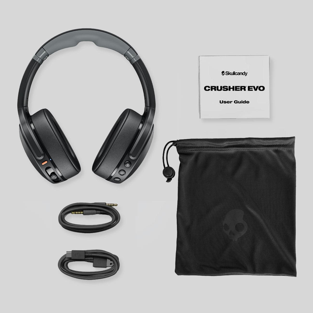 Crusher Evo headphones laid out with the user guide, a satin drawstring bag, a USB-C charging cable and a backup AUX cable