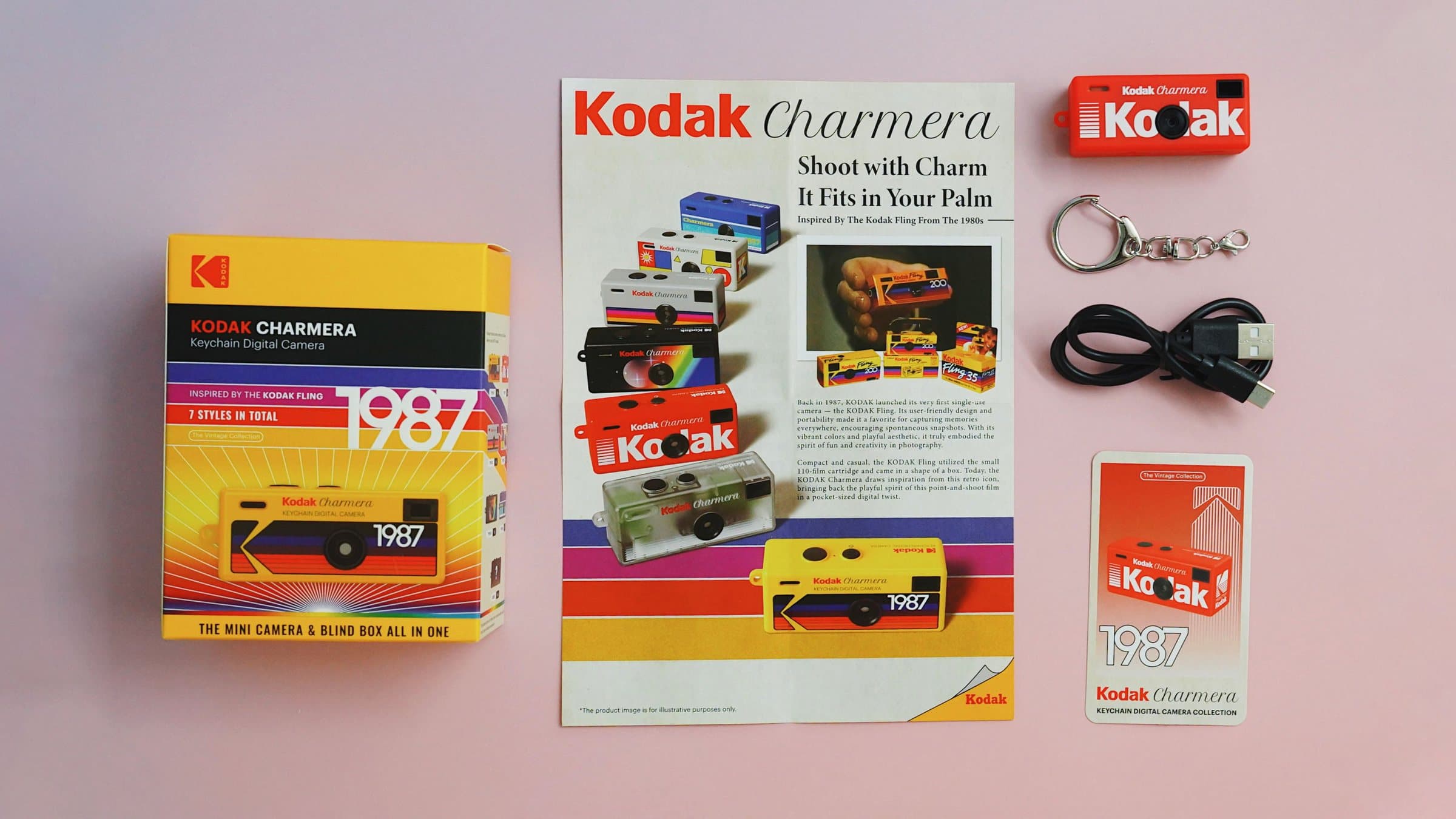 The contents of a Kodak Charmera blind box laid out: the yellow 1987 box, the A5 leaflet, a Charmera camera, the keyring, the USB-C cable and the Charmera ID card